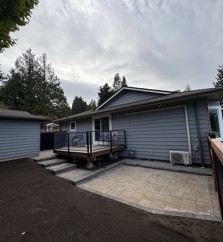 Updated home exterior with a wooden deck, patio, and landscaped yard under a cloudy sky.
