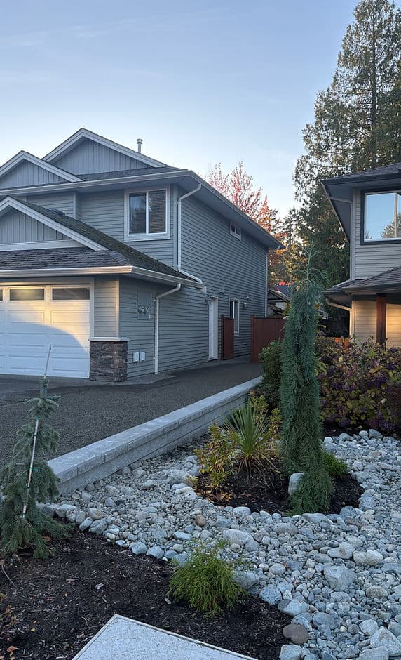 Modern home exterior with landscaped garden, gravel driveway, and evergreen plants.