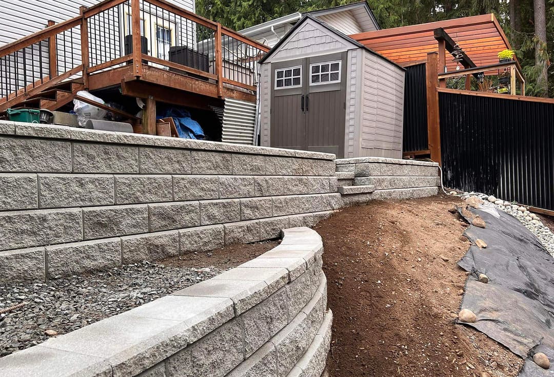 Landscape featuring a stone retaining wall, pathway, and shed in a backyard setting.